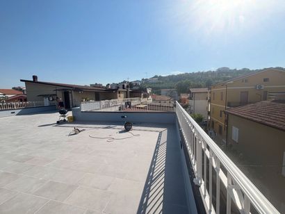 Terrazza sul tetto con ringhiera bianca, affacciata sulle case sotto un cielo azzurro e luminoso