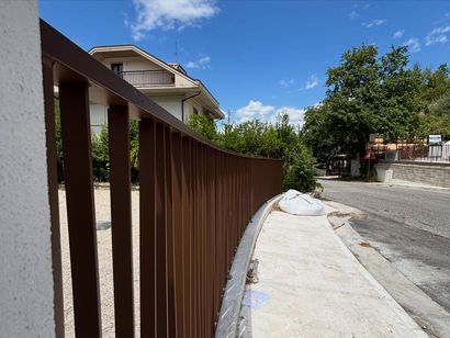 Ringhiera curva in metallo marrone accanto a un marciapiede in cemento su una strada residenziale soleggiata