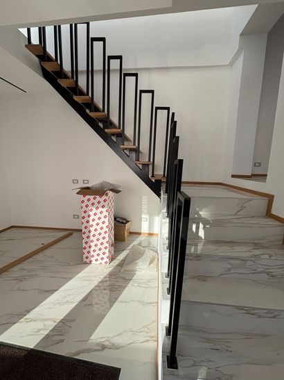 Moderna scala interna con corrimano in metallo nero in un luminoso ingresso con pavimento in marmo