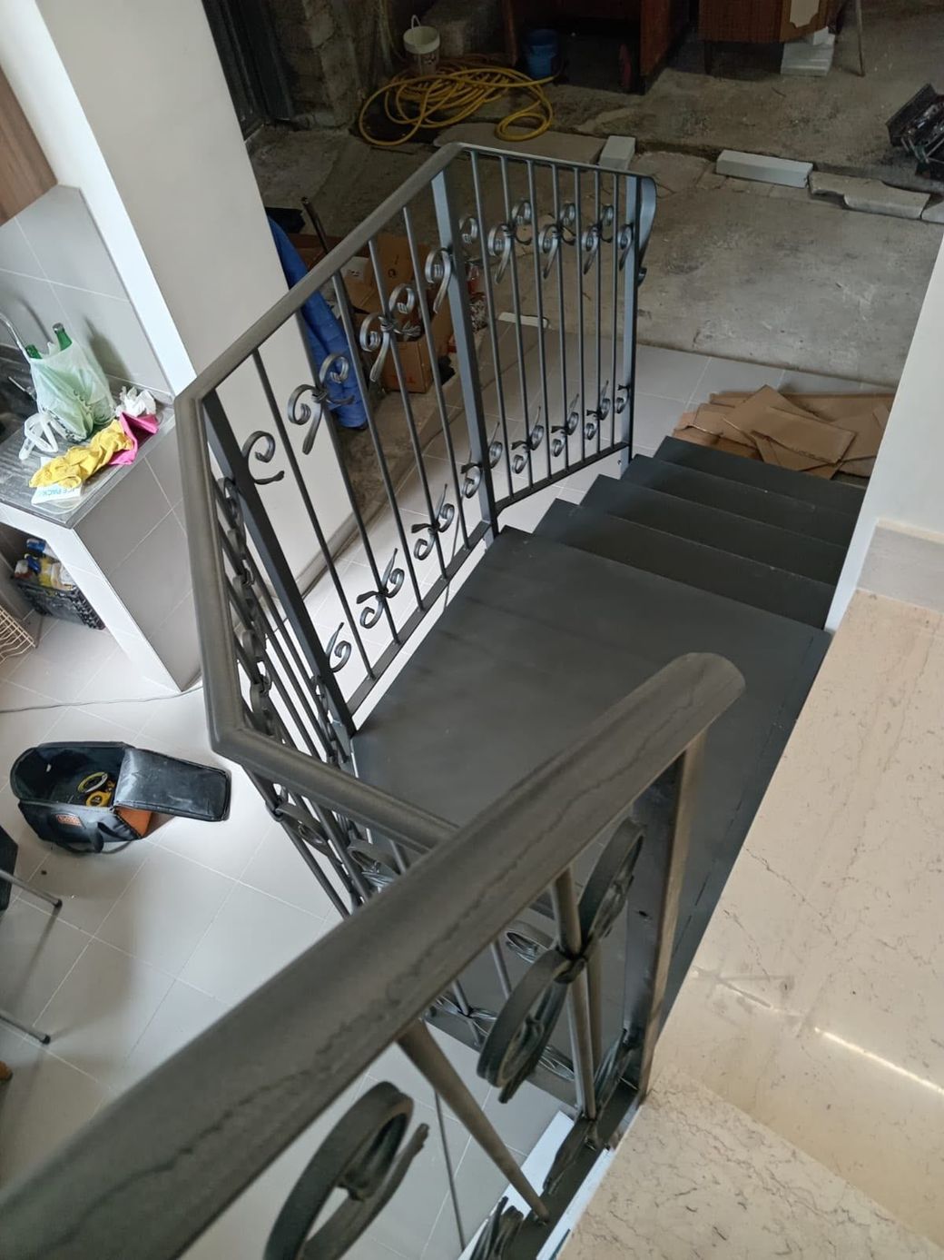 Vano scale interno con ringhiera in metallo nero e pavimenti piastrellati, visto da un pianerottolo superiore.
