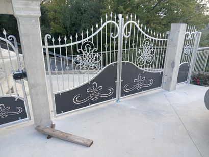 Cancello carrabile in ferro battuto bianco con decorazioni a volute e pilastri in cemento su un vialetto pavimentato.