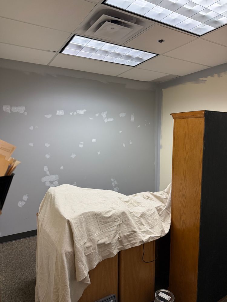 Small office with gray walls, ceiling lights, a covered cabinet, and a tall wooden cabinet.