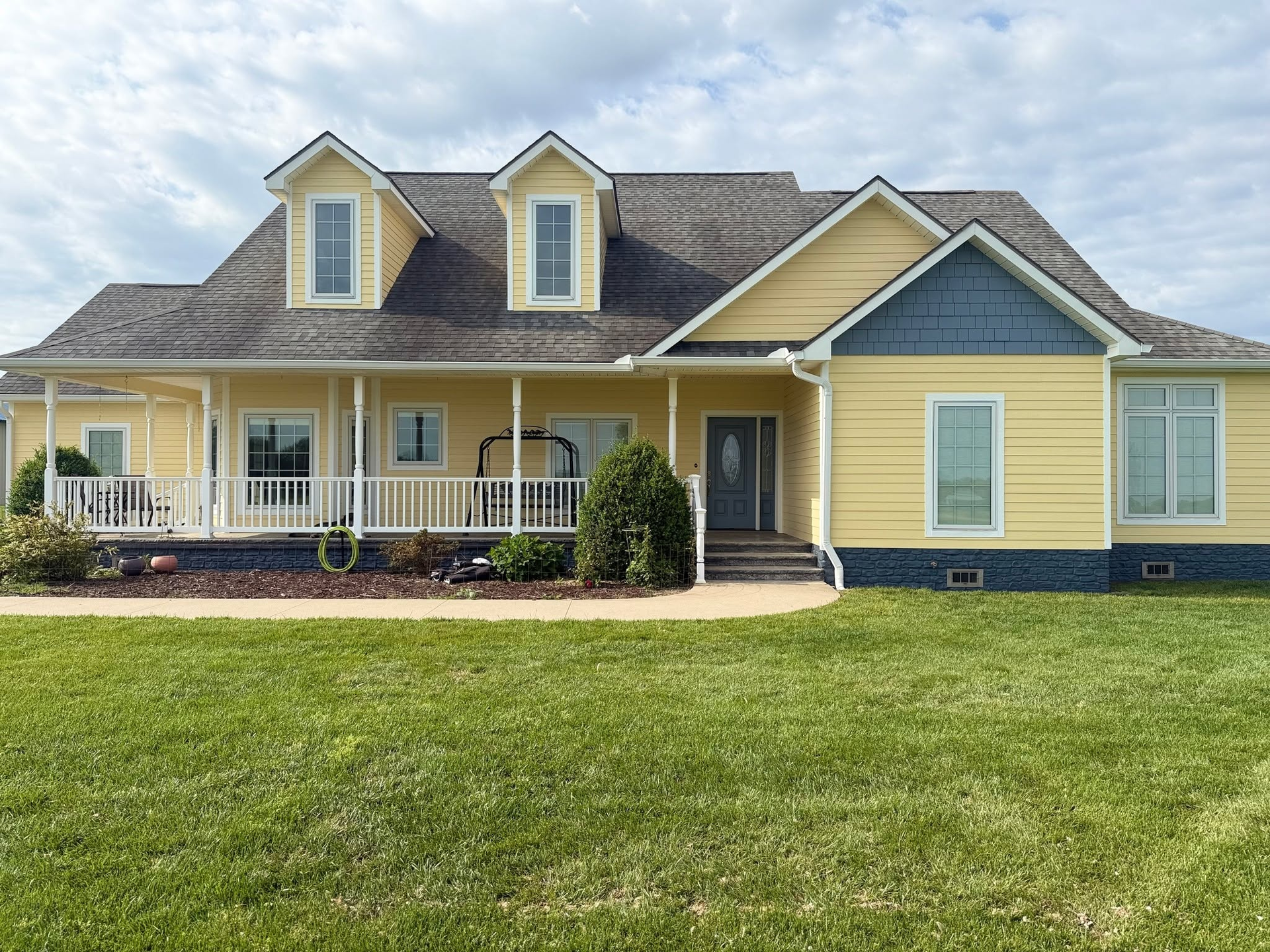 Yellow house with a front porch, dormer windows, and a large green lawn
