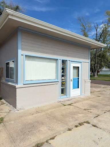 Small beige-and-blue kiosk building with windows, glass door, and a concrete lot under a clear sky