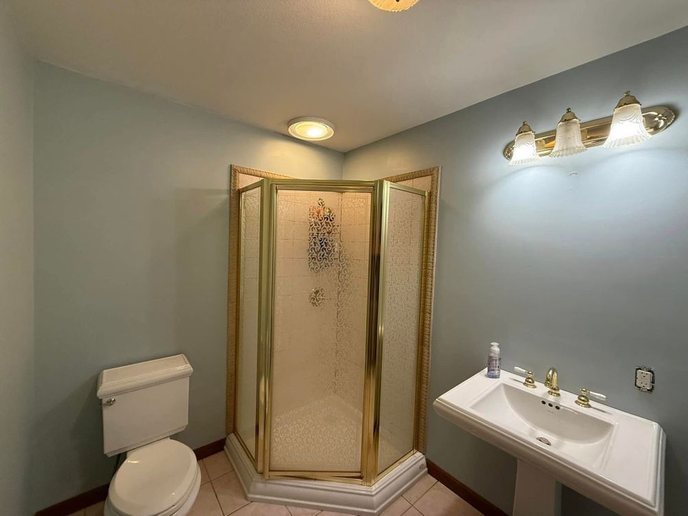 Small bathroom with a glass shower, toilet, white vanity, and light blue walls.