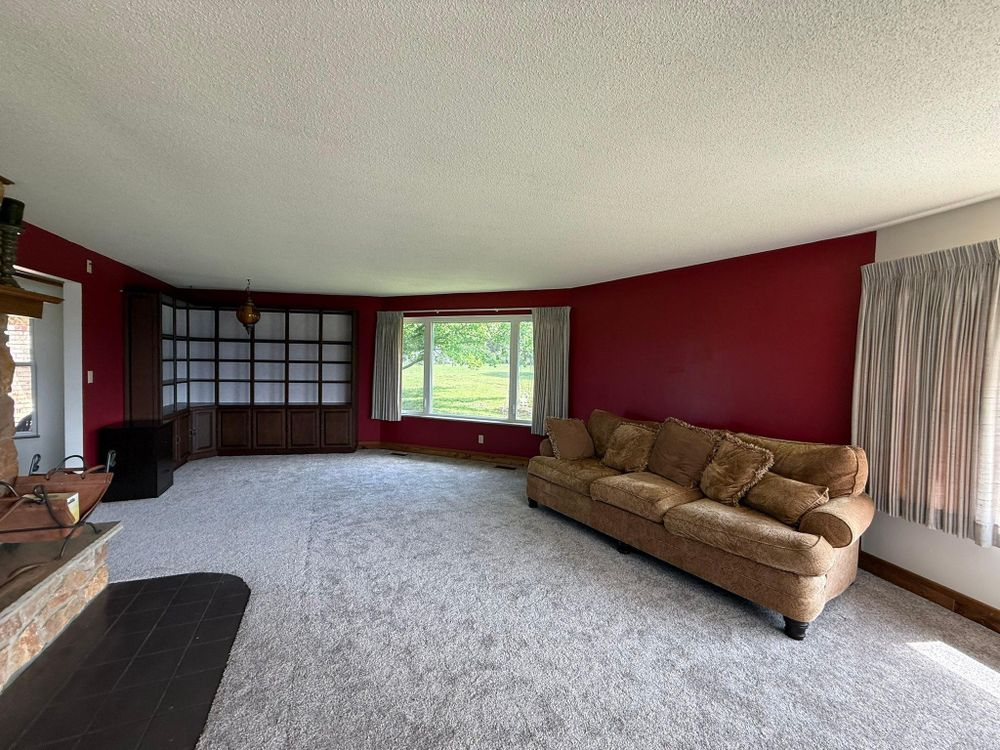 Spacious living room with burgundy walls, beige sofa, gray carpet, and large window with curtains.
