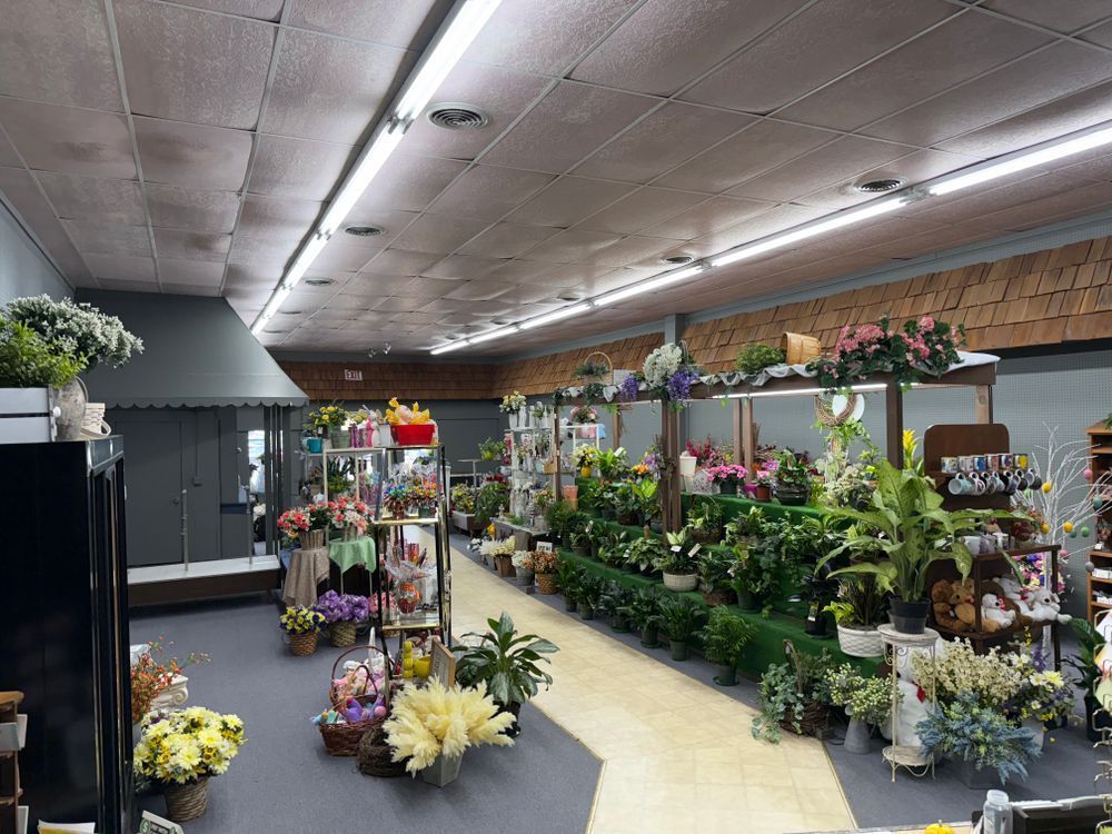 Indoor flower shop aisle lined with colorful potted plants and floral arrangements under bright lights