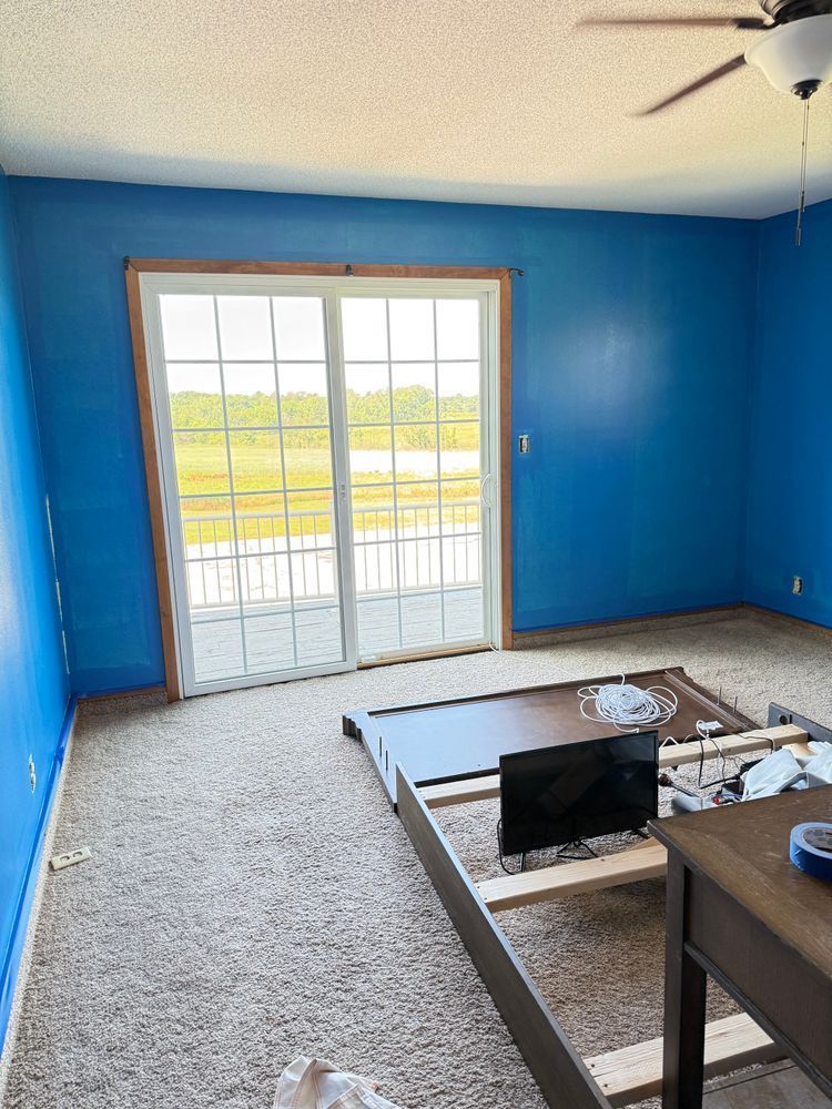 Blue room with sliding glass doors, carpeted floor, and an open floor section exposing framing.
