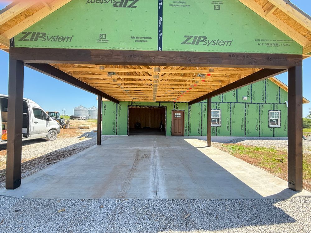 Open-front house under construction with green sheathing, wood roof framing, and concrete floor