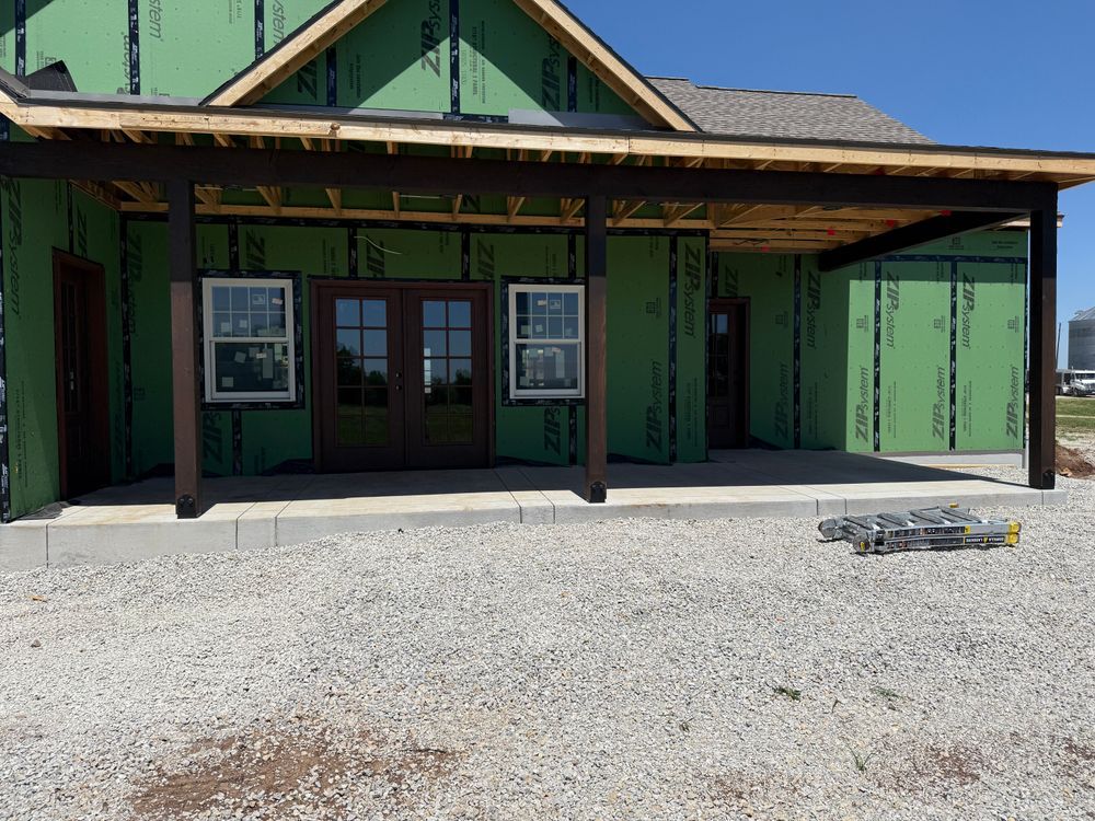 Green building with a covered porch, double doors, and gravel foreground under a clear sky