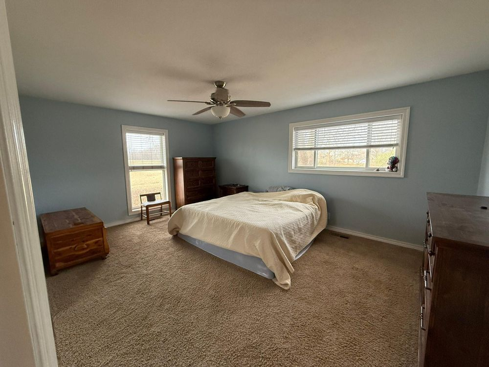 Bedroom with a bed, dresser, chest, and ceiling fan in soft blue-gray tones.