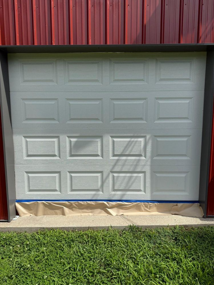 Closed white garage door with blue painter’s tape at the bottom, under a red roof, beside green grass.