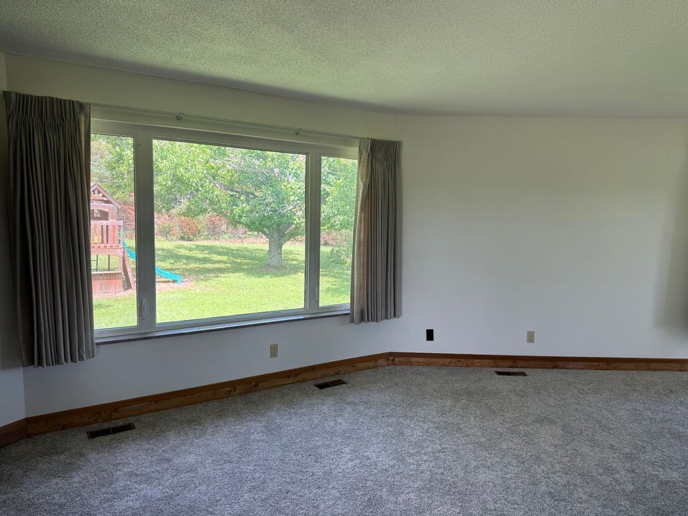 Empty living room with gray carpet, large window, and view of a green backyard