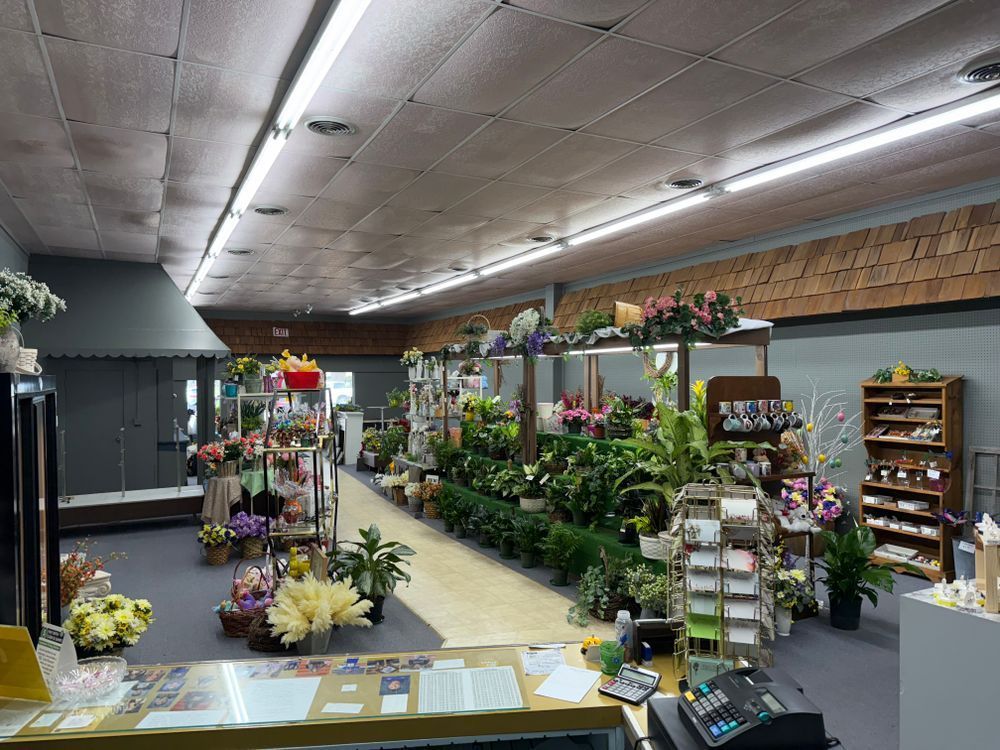 Indoor flower shop with rows of potted plants, bouquets, and floral displays along a long aisle.