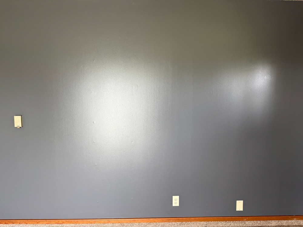 Empty room with a dark gray wall, wood floor trim, and three outlet covers.