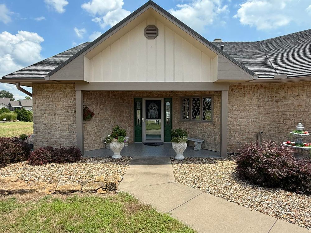 Front entrance of a brick house with a covered porch, concrete walkway, and landscaped yard