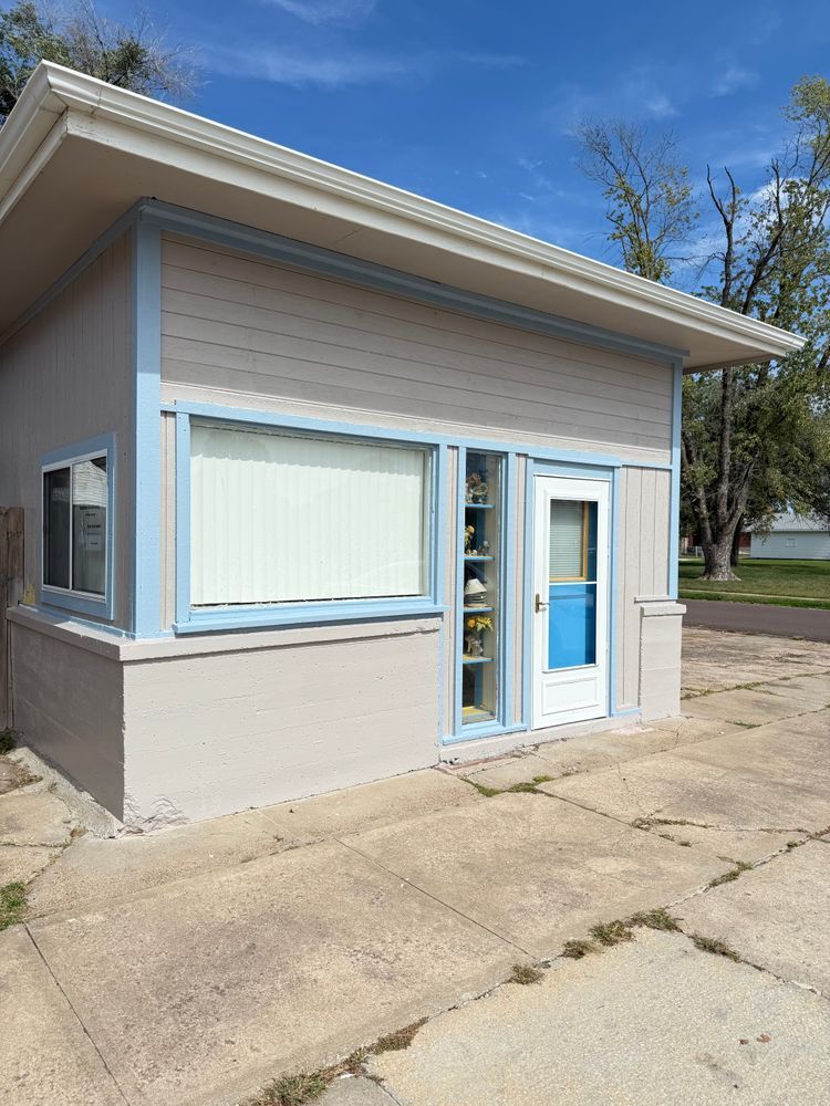 Small beige storefront with blue trim and large windows on a sunny day