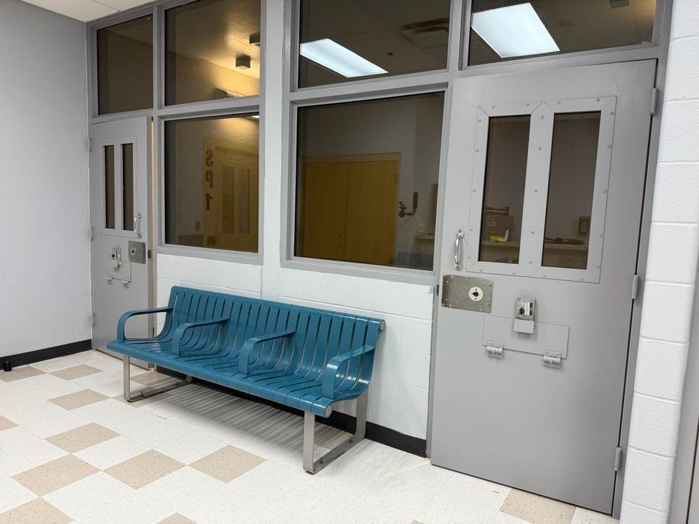 Empty hallway with a blue bench beside gray doors and windows.