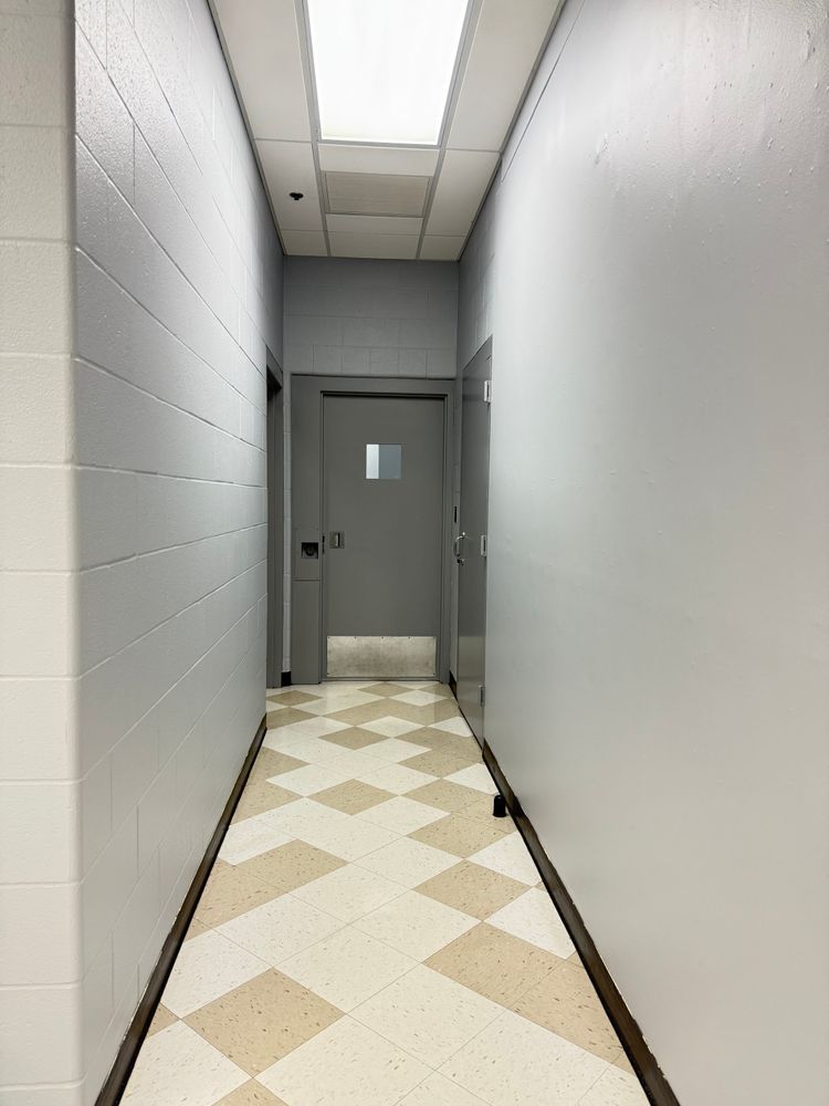 Narrow white hallway with a gray door at the end and a cream diamond-patterned floor.