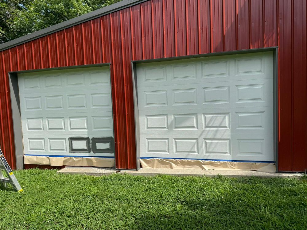 Red barn-style garage with two white doors and red siding, viewed from the front across a grassy lawn.