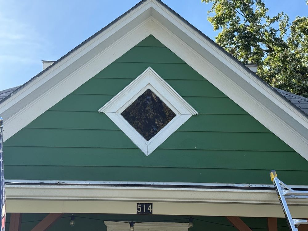 Green house gable with white trim and diamond window under a blue sky