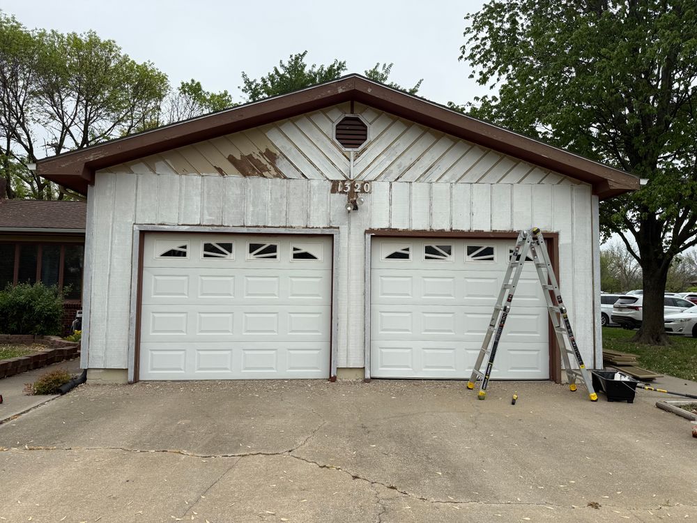 Two-car garage with white doors; ladder leans against the right side of the house.