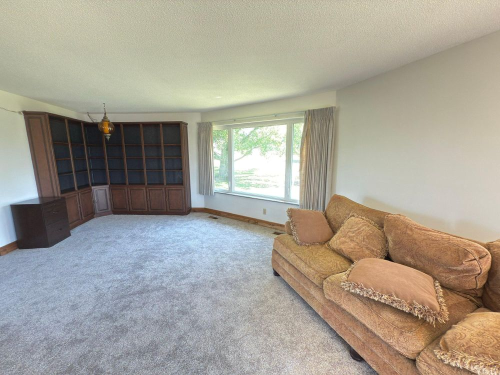 Living room with beige sofa, large window, gray carpet, and built-in wooden shelving