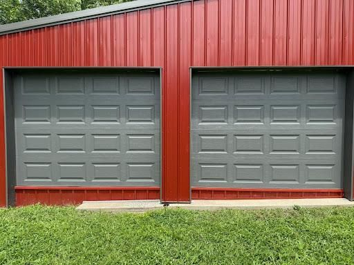 Two gray garage doors on a red building with a green lawn in front.
