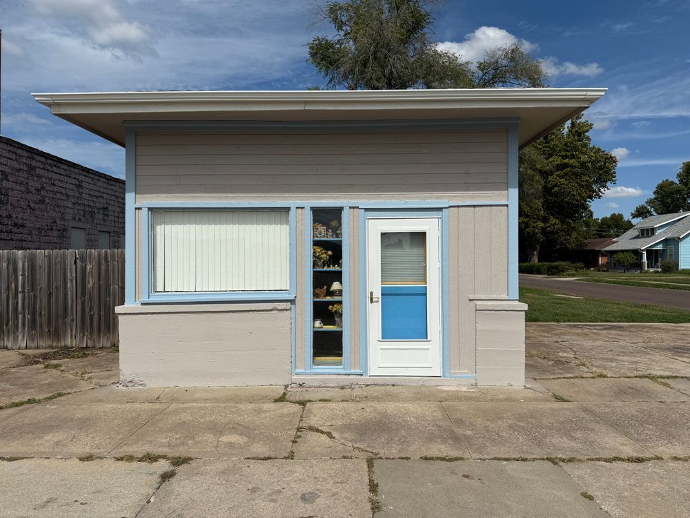 Small beige storefront with large windows, glass door, and flat roof on a quiet street.