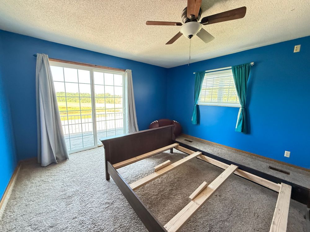 Bright blue bedroom with a disassembled bed frame, ceiling fan, and sliding glass doors to a patio