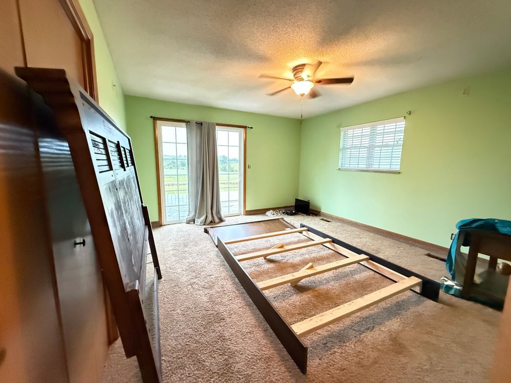 Empty bedroom with green walls, carpet, ceiling fan, and exposed floor joists near sliding glass doors.