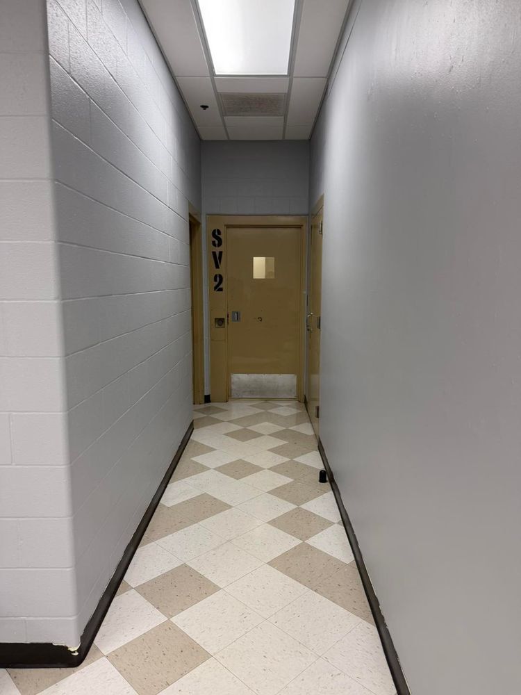 Narrow hallway with white walls, tiled floor, and a beige door at the end.