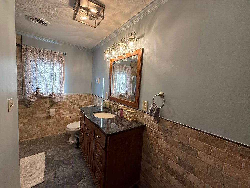 Small bathroom with dark vanity, large mirror, brick tile walls, window, toilet, and shower curtain.