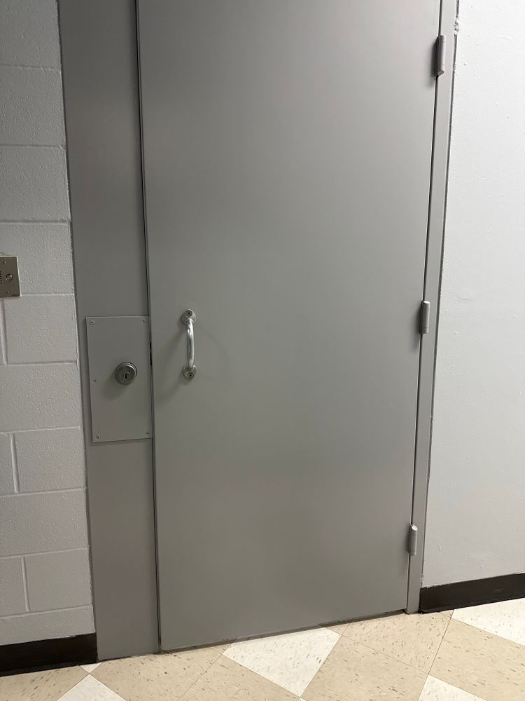 Gray metal door in a hallway beside a white cinderblock wall and tiled floor.