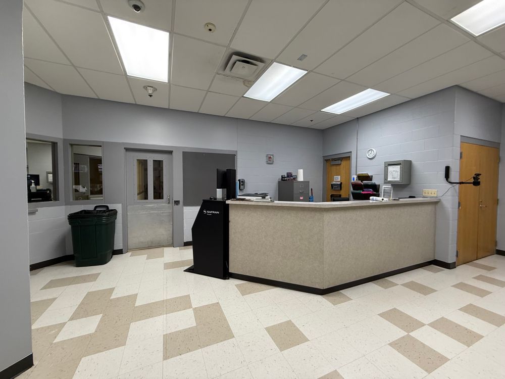Empty office lobby with a reception desk, gray walls, fluorescent lights, and a tan checkered floor.