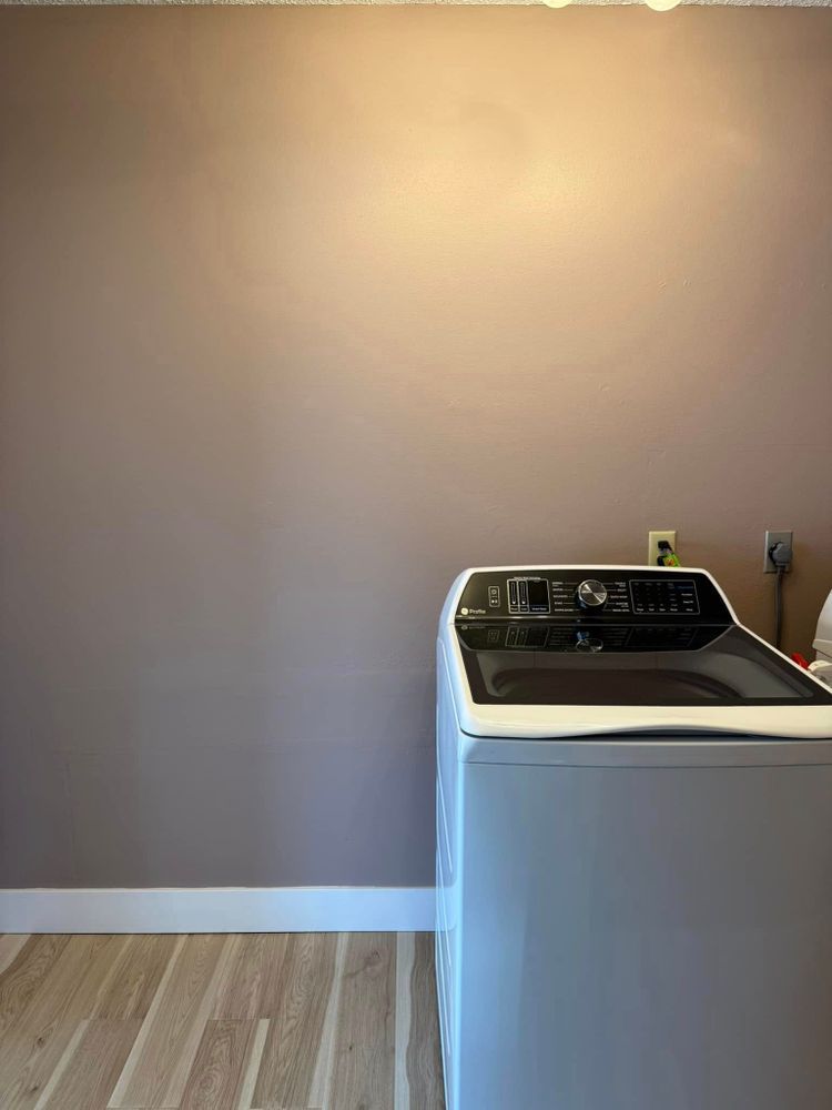Empty laundry room with beige walls, wood floor, and a white washer under a wall outlet.