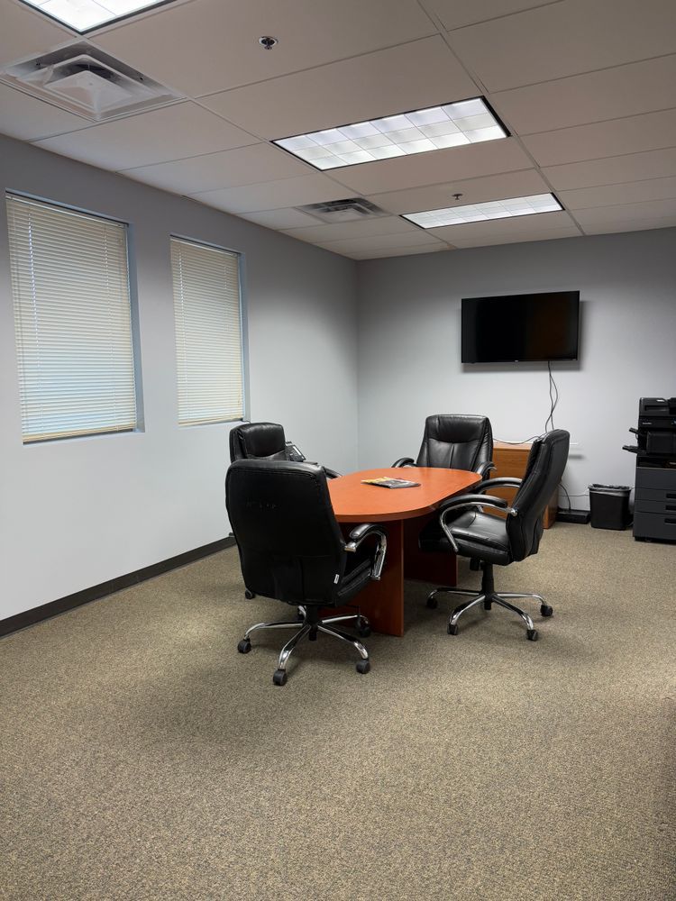 Empty conference room with round orange table, black chairs, wall-mounted TV, and carpeted floor