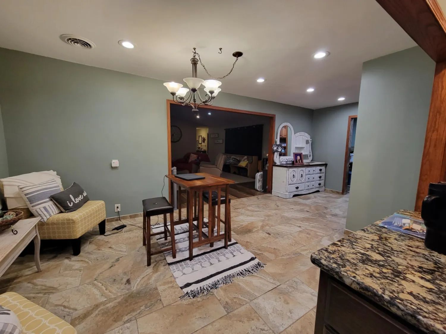 Open living and dining area with tiled floor, chandelier, chairs, and granite countertop