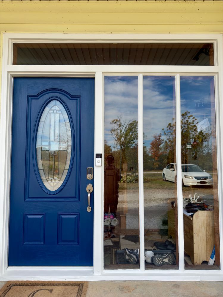 Blue front door with oval glass inset beside a glass sidelight on a yellow house porch
