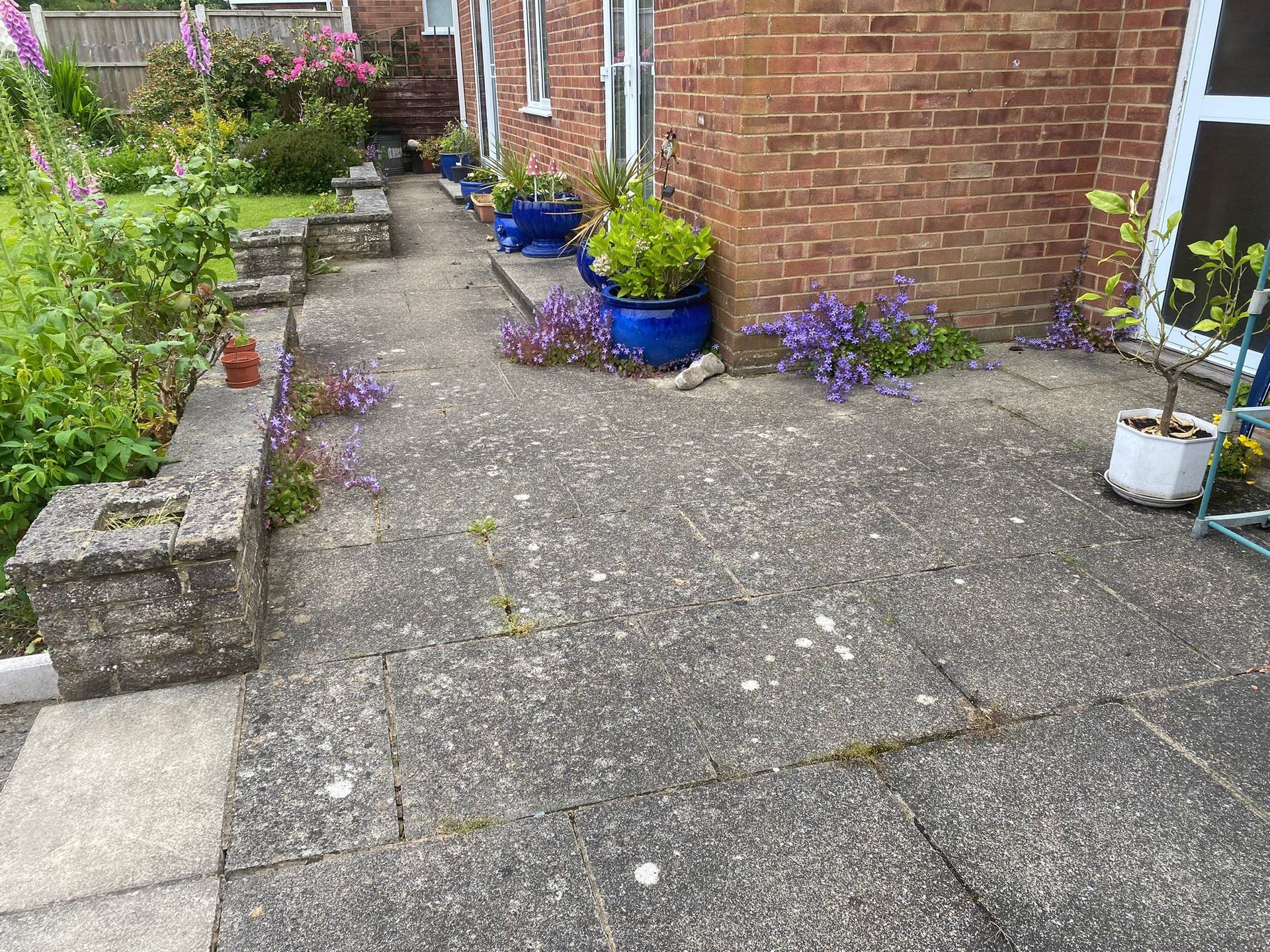 A patio with potted plants and flowers in front of a brick house.