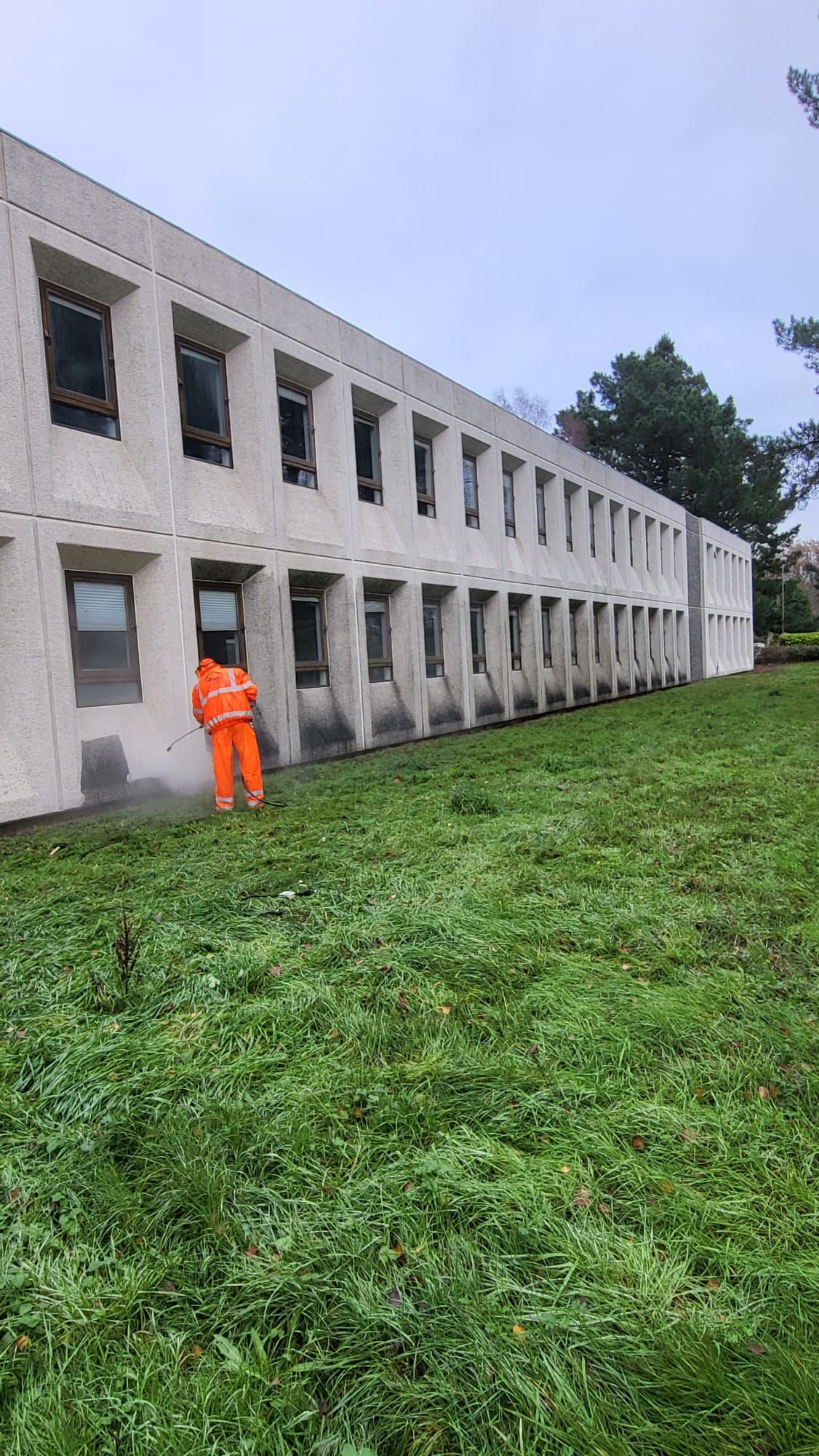 A man in orange safety suit is cleaning windows in front of a building.