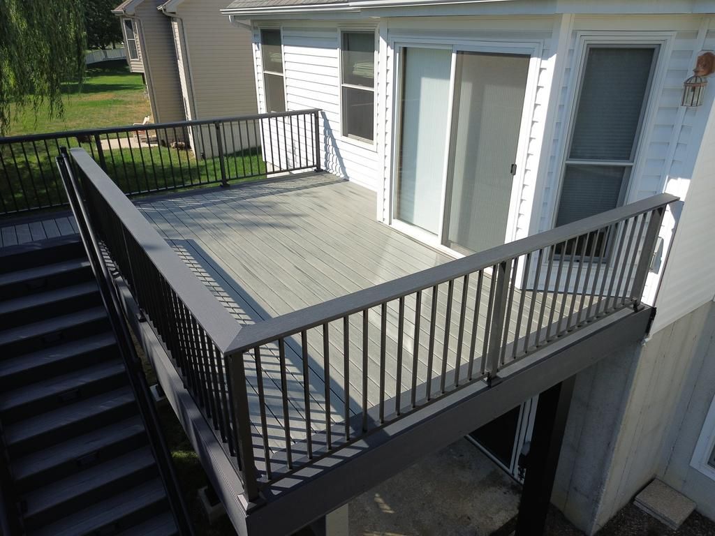 Composite deck with black railing and steps leading down. Adjacent to a white house with sliding door.