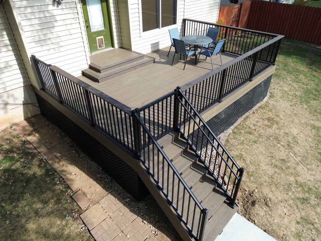 Wooden deck with black railing and steps; a table and chairs sit on the deck.