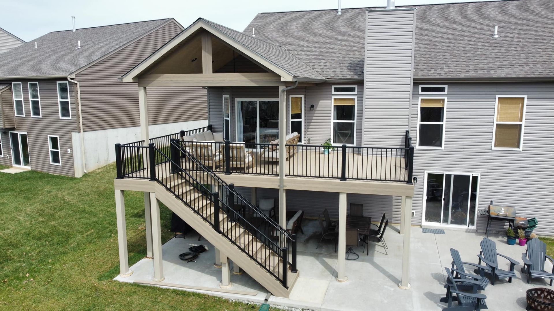 A multi-level deck with stairs. A covered upper deck, lower patio. Houses surround on a grassy lawn.