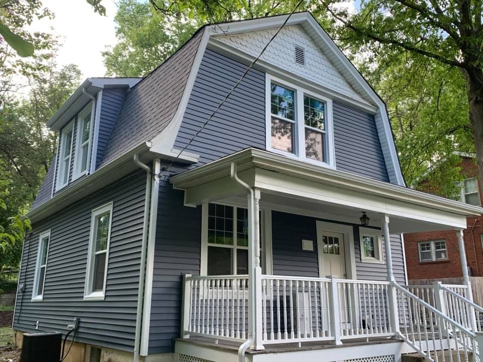 Blue house with white trim, porch, and a dormer. It's set amongst trees.