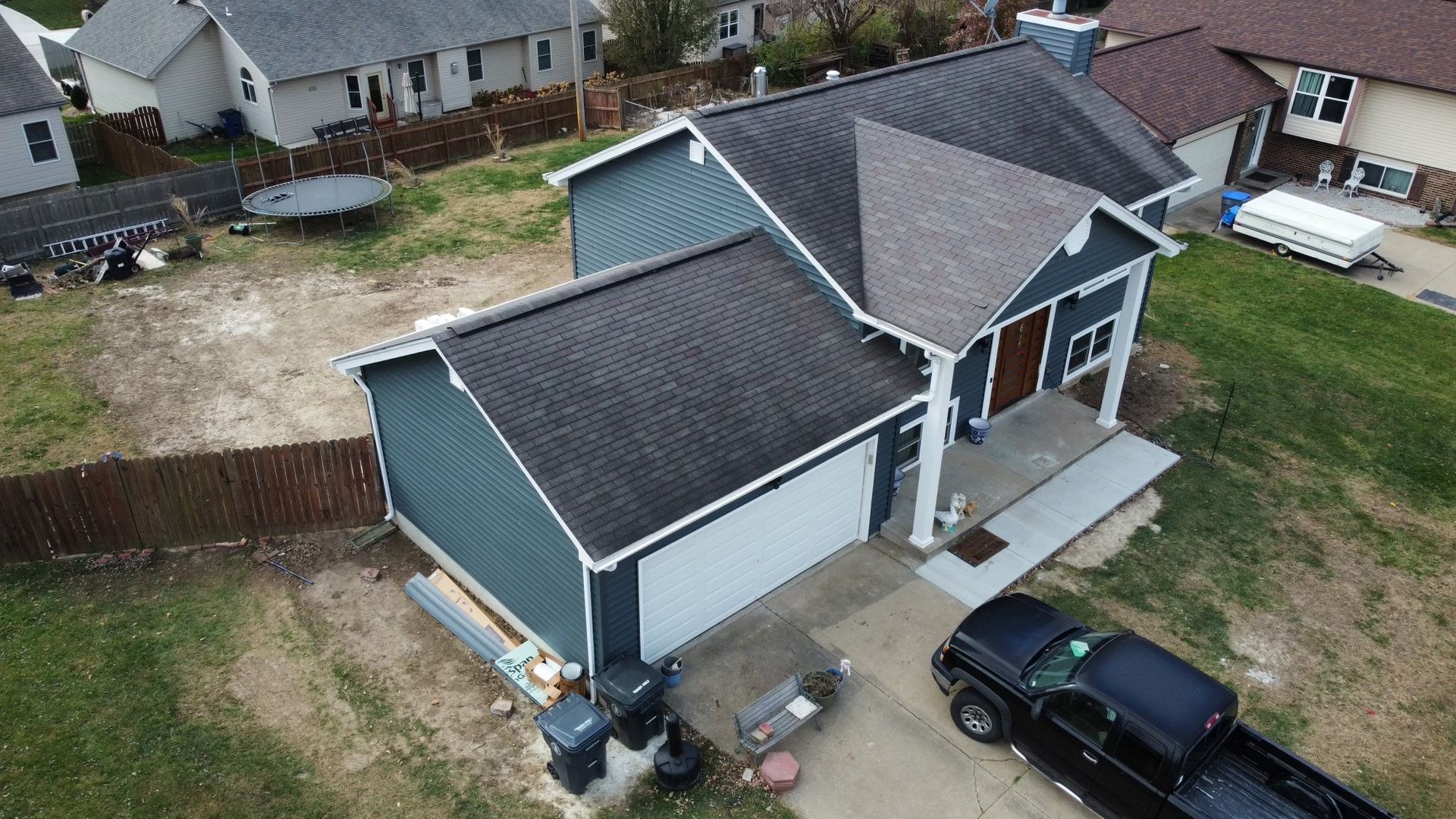 Blue house with attached garage, brown roof, black pickup truck parked in front.