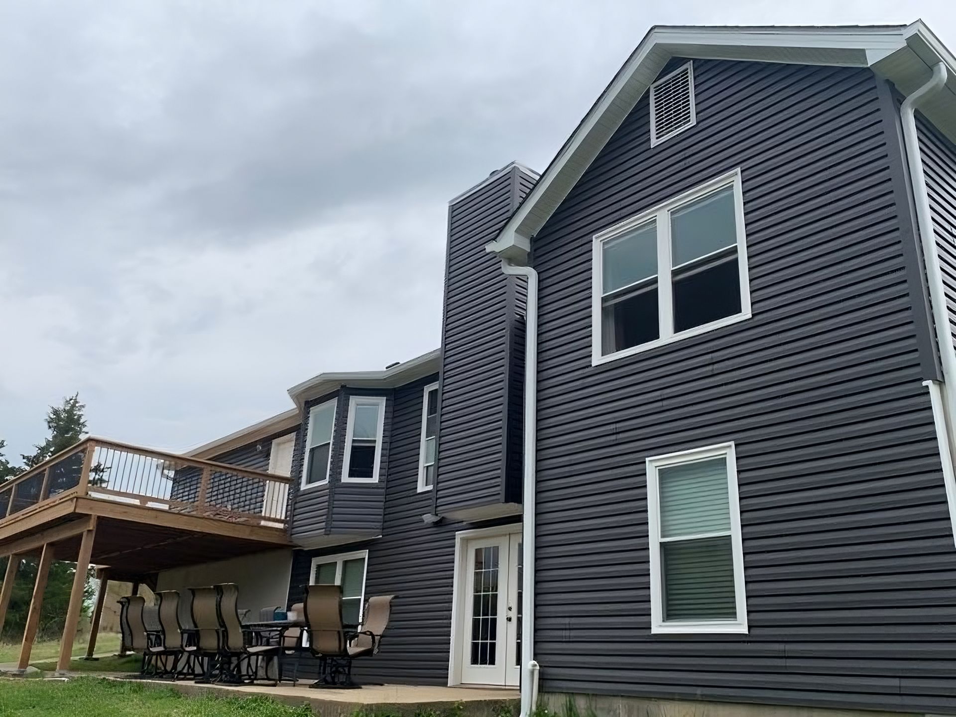 Two-story house with dark gray siding, a deck, and chimney under a cloudy sky.