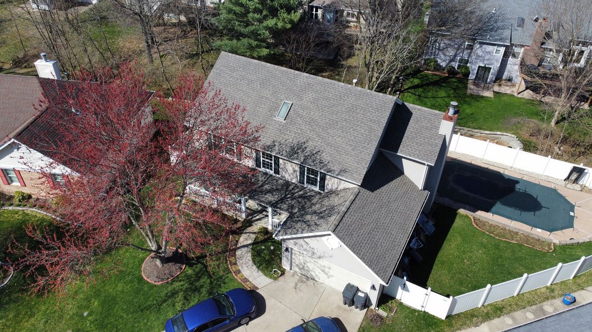 Aerial view of a gray two-story house with a pool in a suburban setting. A blooming red tree is in the yard.