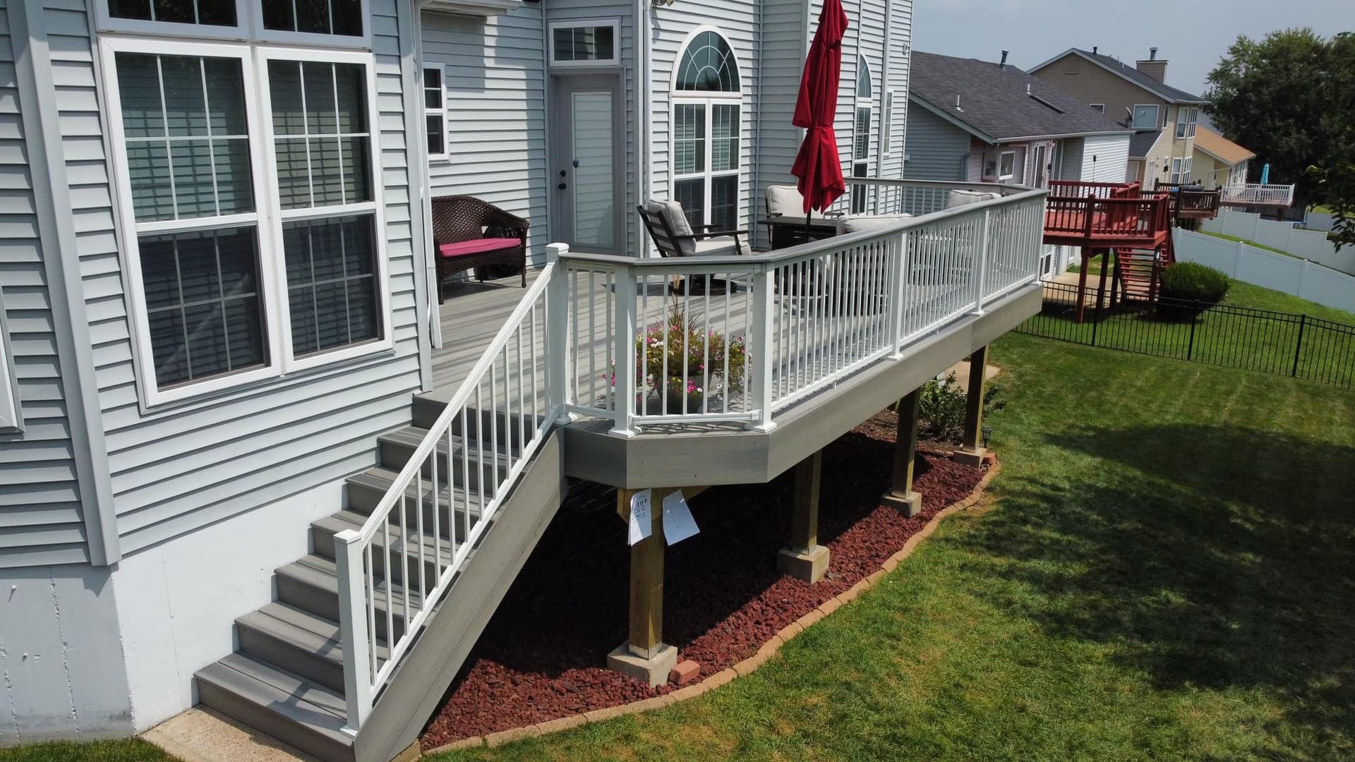 Deck with white railing and stairs on a house with a red umbrella.