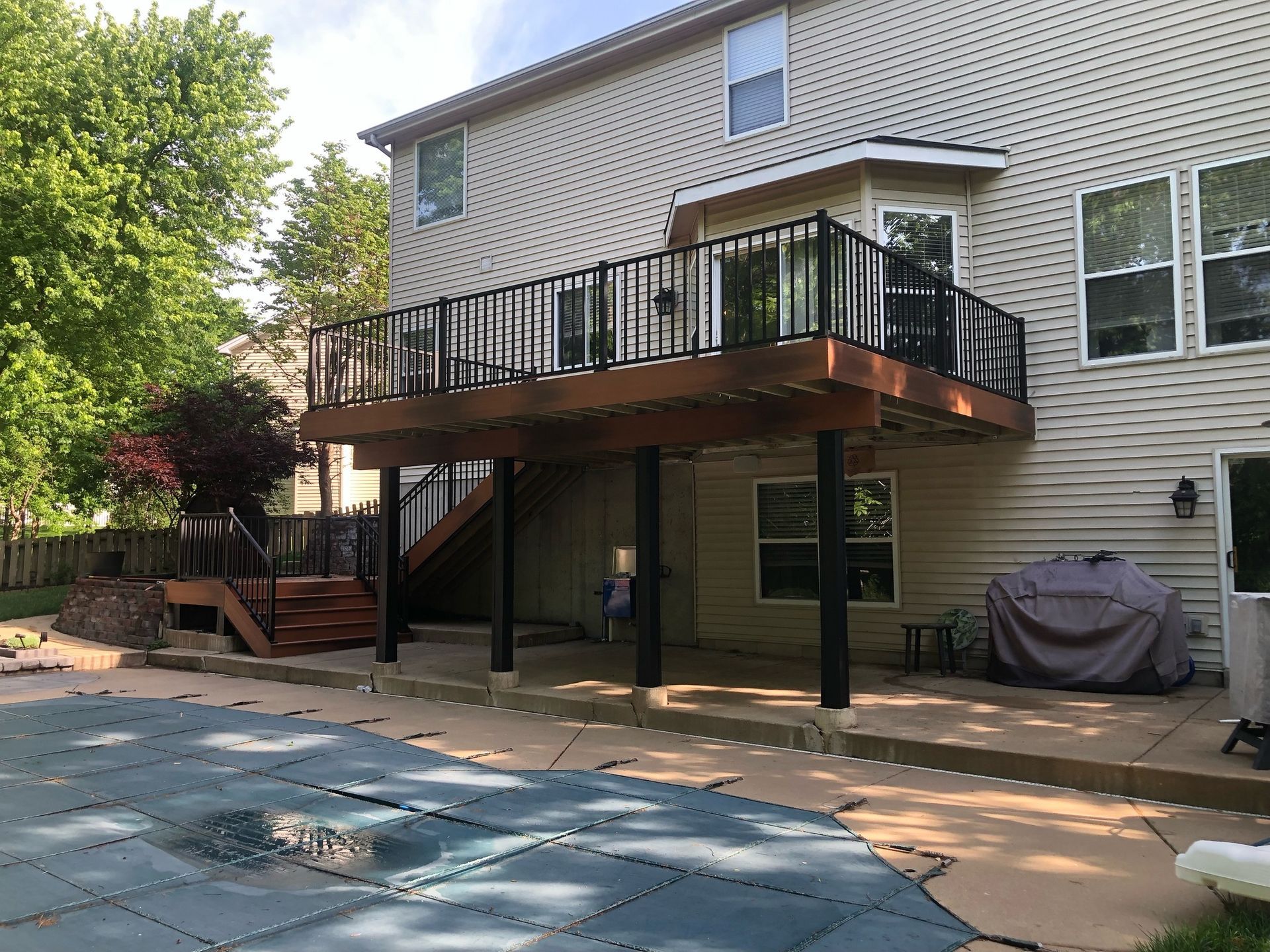 Backyard view: Elevated deck with black railing, overlooking a pool. House has beige siding.